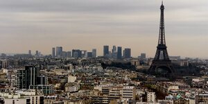 La tour eiffel se dresse dans le ciel de paris avec les batiments du centre d'affaires de la defense en arriere-plan.